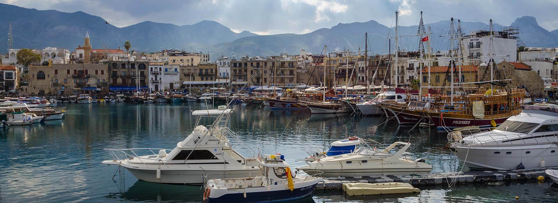 Harbor full of color boats on clear shallow waters with old buildings all around.